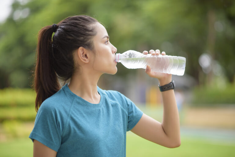Fitness woman is drinking water after workout in park