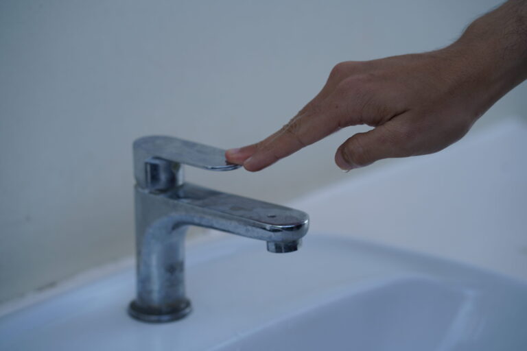 Close-Up of a Hand Reaching for a Chrome Faucet in a Modern Bathroom Setting, Indicating Desire for Clean Water or Personal Hygiene