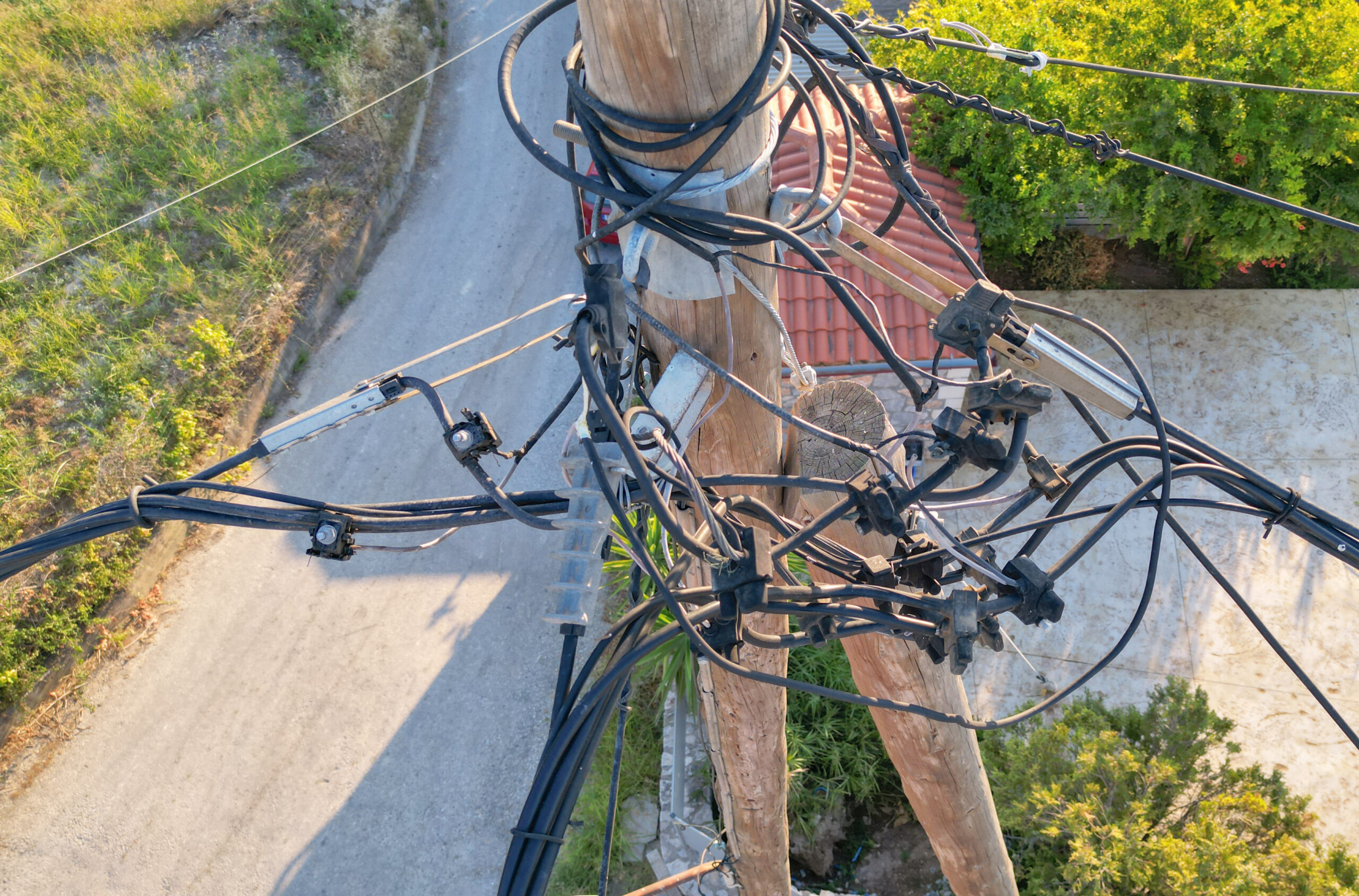 Chaotic wires on old pole with Cretan nature background, outdated electricity transmission method.